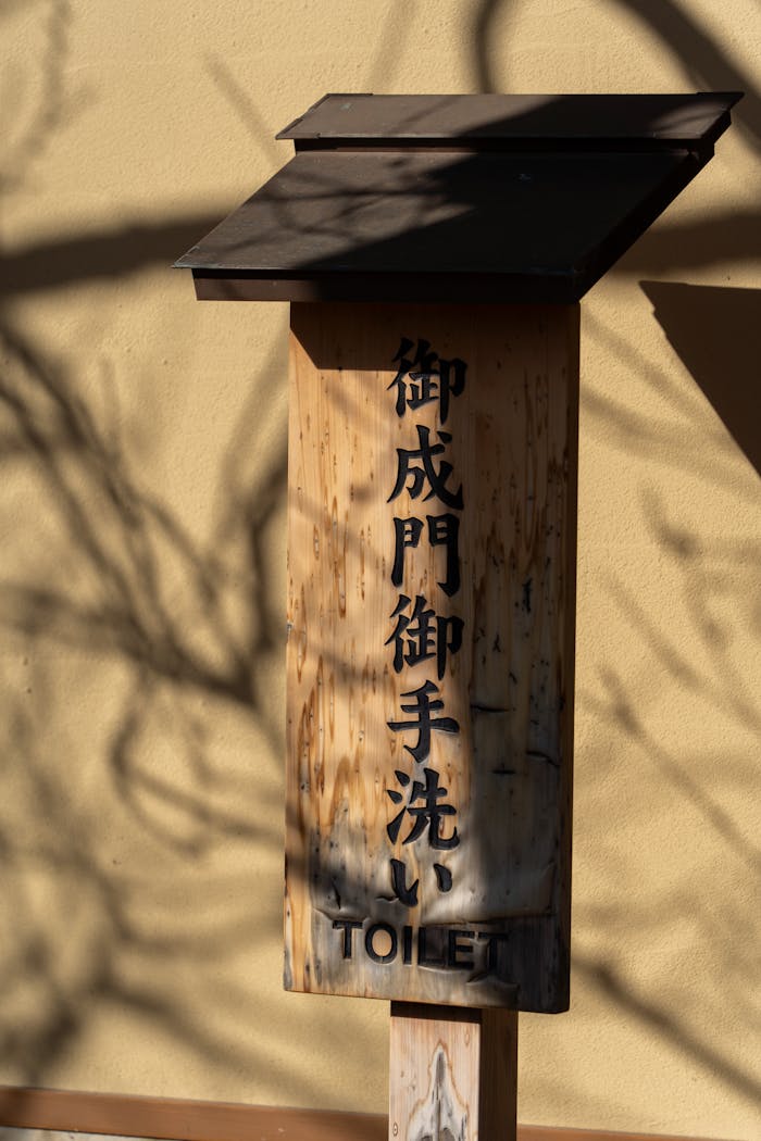 hero-img-02 Wooden toilet sign with Japanese characters in sunlight and shadows.